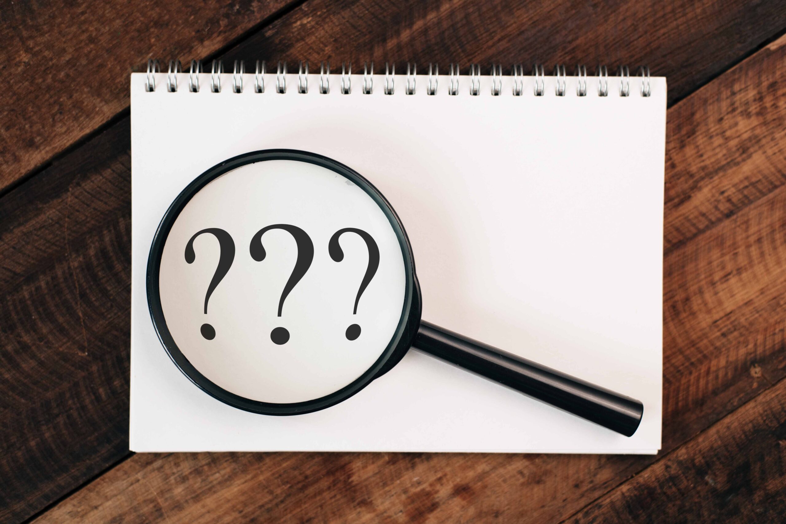 ノートに書かれたクエスチョンマークの上に置かれた虫眼鏡